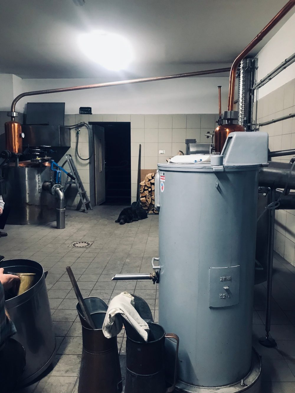 Pálenice s měděnými kotli a destilační kolonou, na podlaze konve na destilát